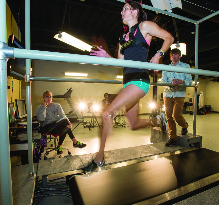 Lindsey Hall ’14, a former Montana Grizzly track and field star who now trains professionally with the Mountain West Track Club, runs on a high-speed force treadmill inside UM’s Biomechanics Lab, which is directed by Professor Matt Bundle, right. UM senior Madi Worst, left, and graduate student Michelle Buechner, rear, control the treadmill and measurement tools through computers.